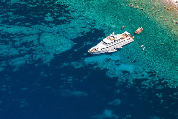 Luxury white pleasure yacht anchored near rocky coast of Corsica island, birds eye view