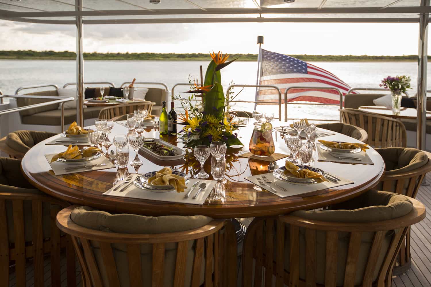 a table set for dinner on the aft deck of a yacht with the sun setting behind