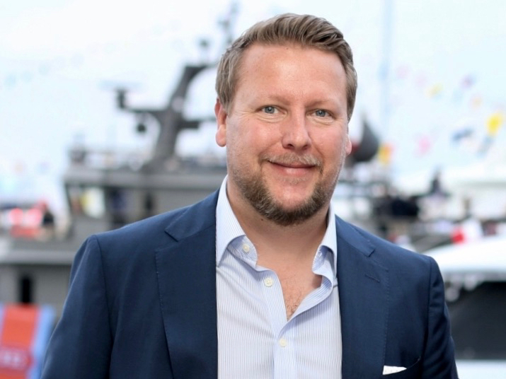 main in suit smiling in front of blurred yachts