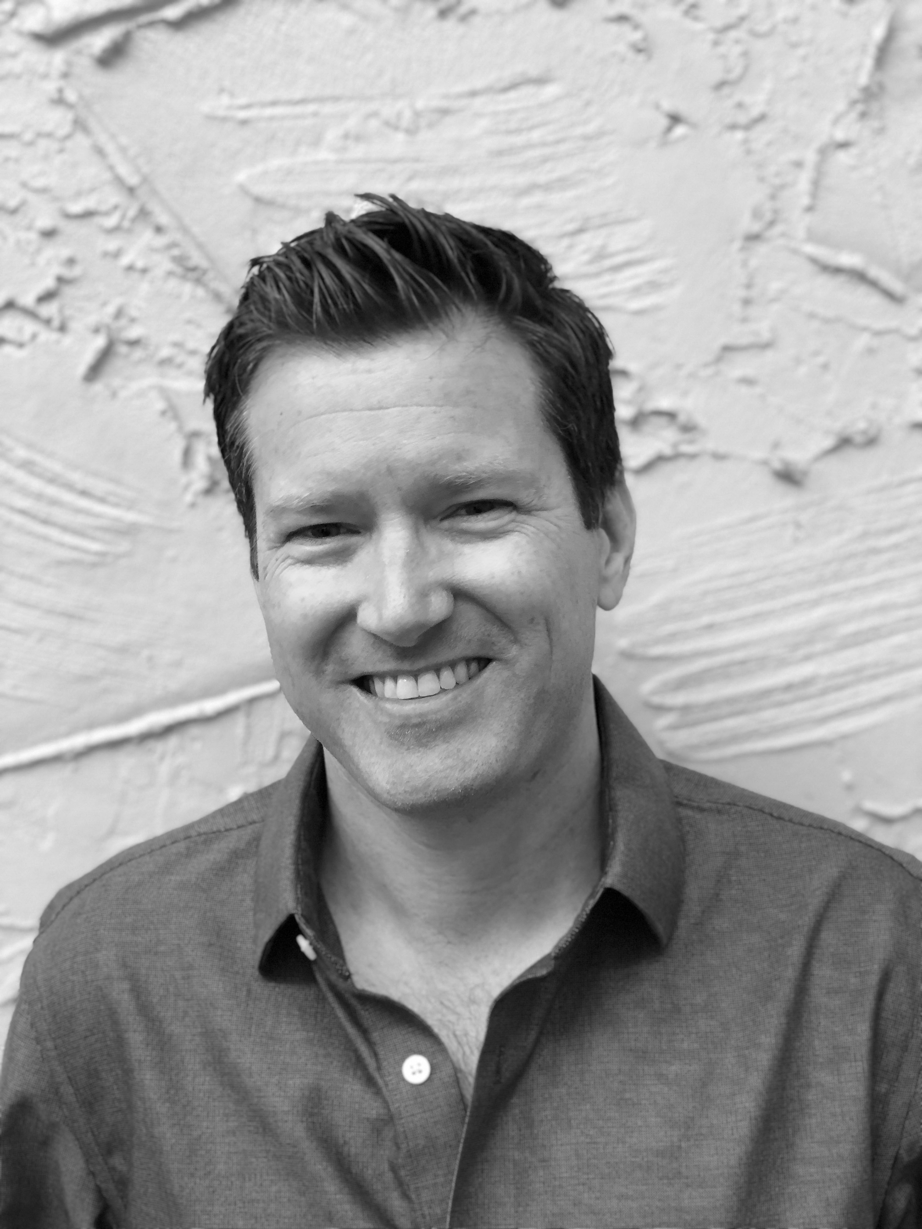 man smiling in front of brick wall