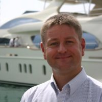 man smiling on dock in front of large white yacht