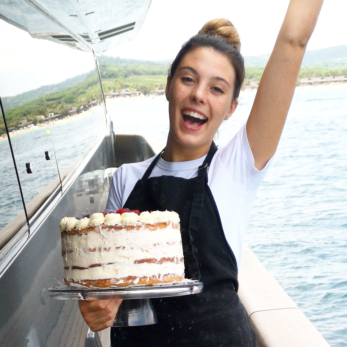 young blonde female yacht chef Jessica Alcock holding a cake on a yacht