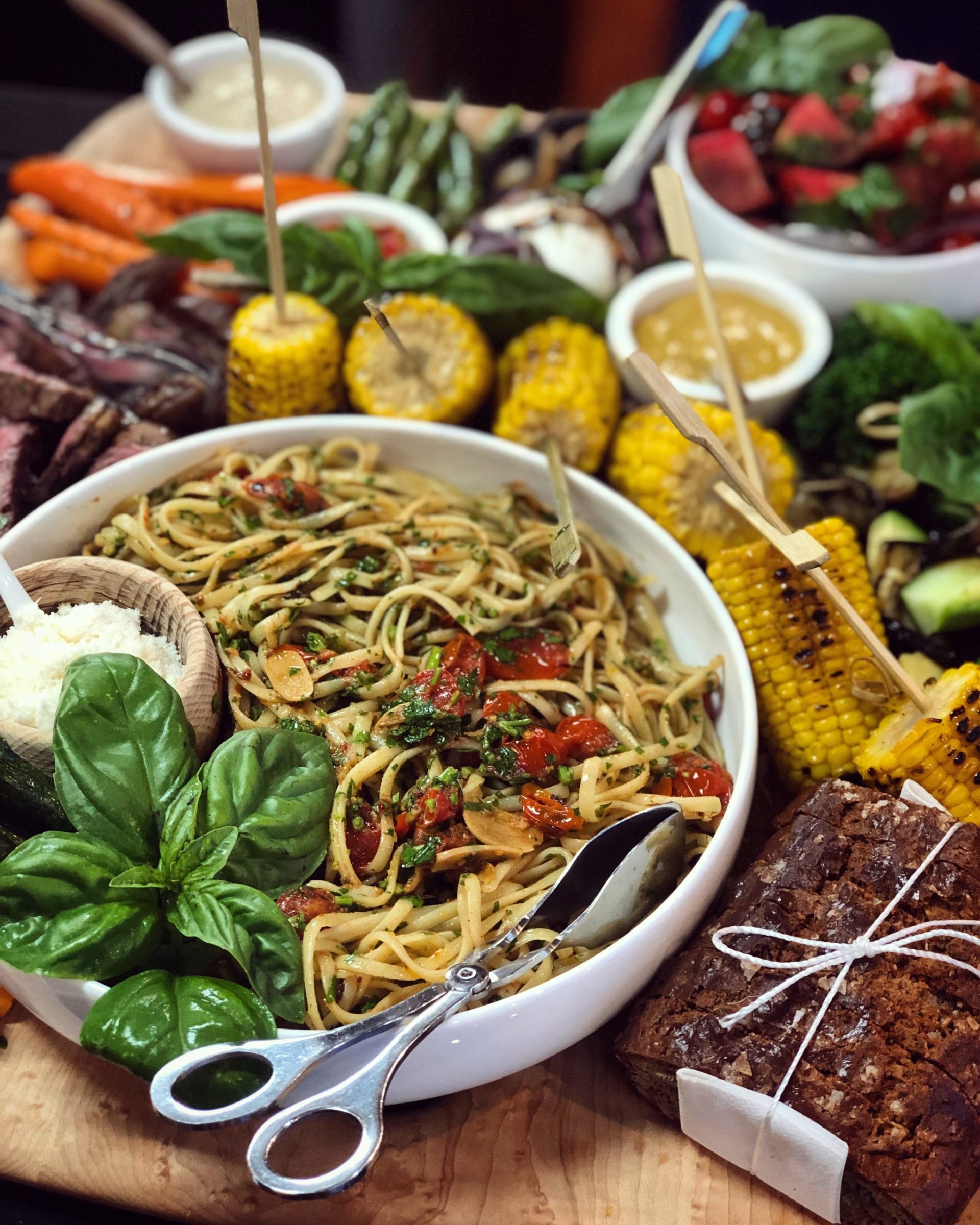 a display of food, big bowl of fresh spaghetti and barbecue corn and bread and salad