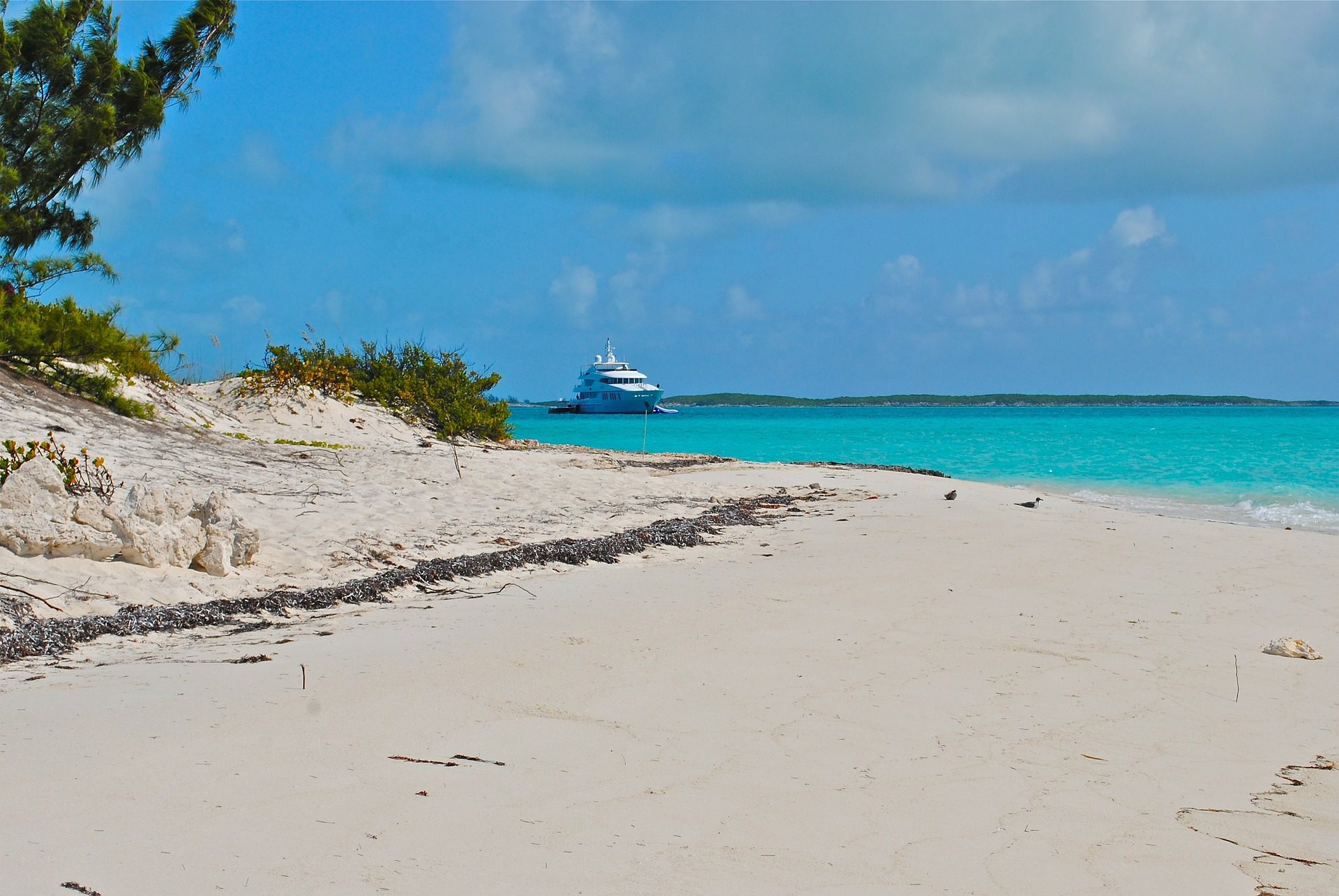 Superyacht in distance with white sand beach in foreground. Image by Lisa Larsen from Pixabay