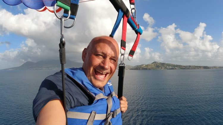 man paragliding in St Kitts with ocean and mountains in background