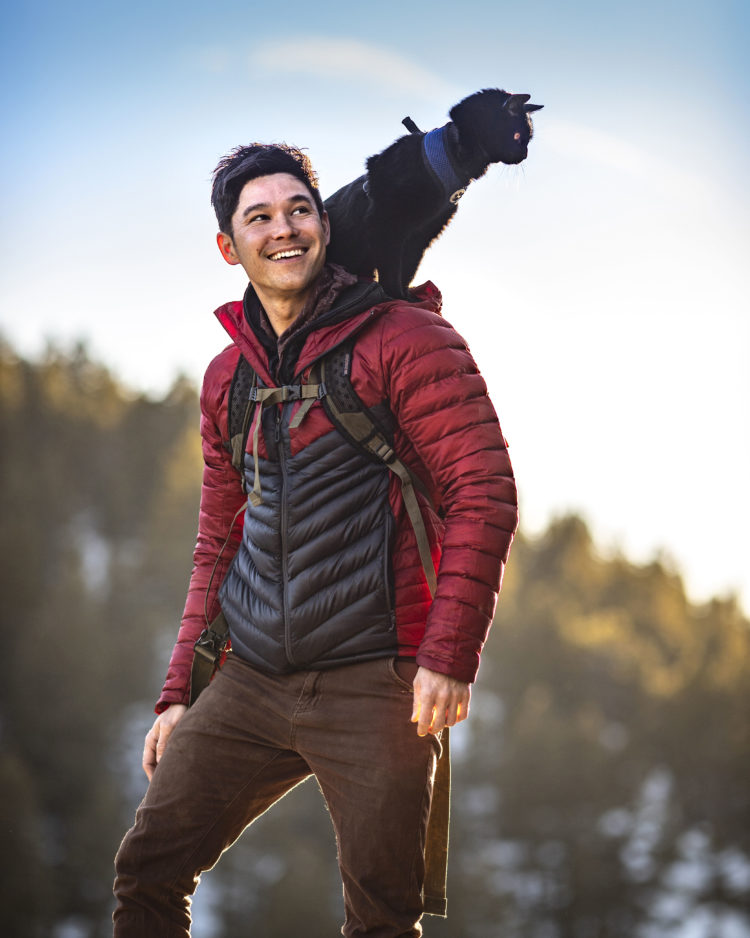 Film director JJ Yosh stands on a mountainside with his cat perched on his shoulder