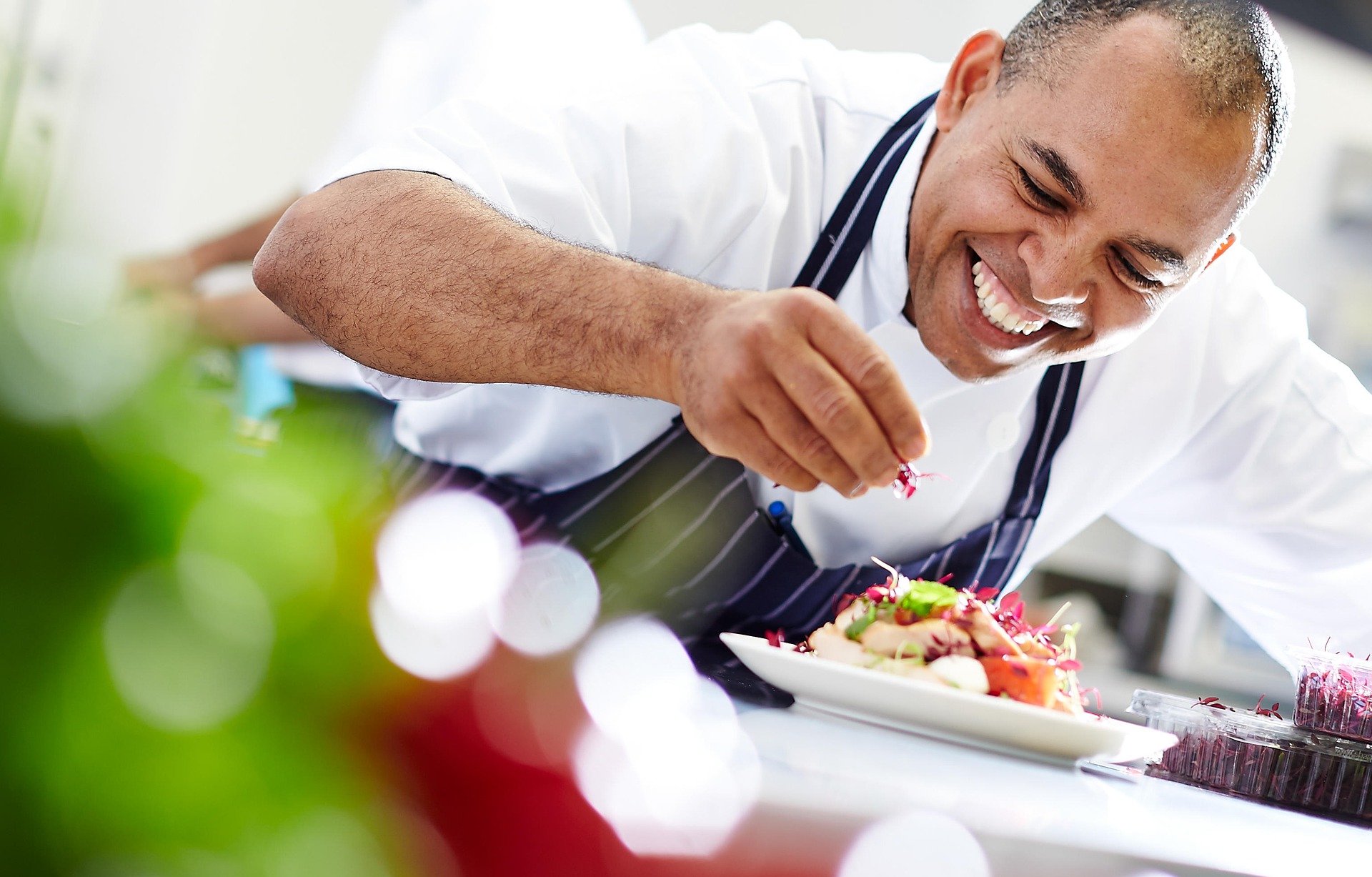 Male chef smiling as he puts the finishing touches on a dish