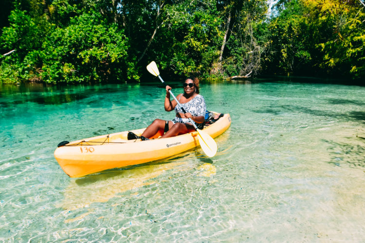 A Black woman paddling in a yellow kayak down the Weeki Wachee River in Florida