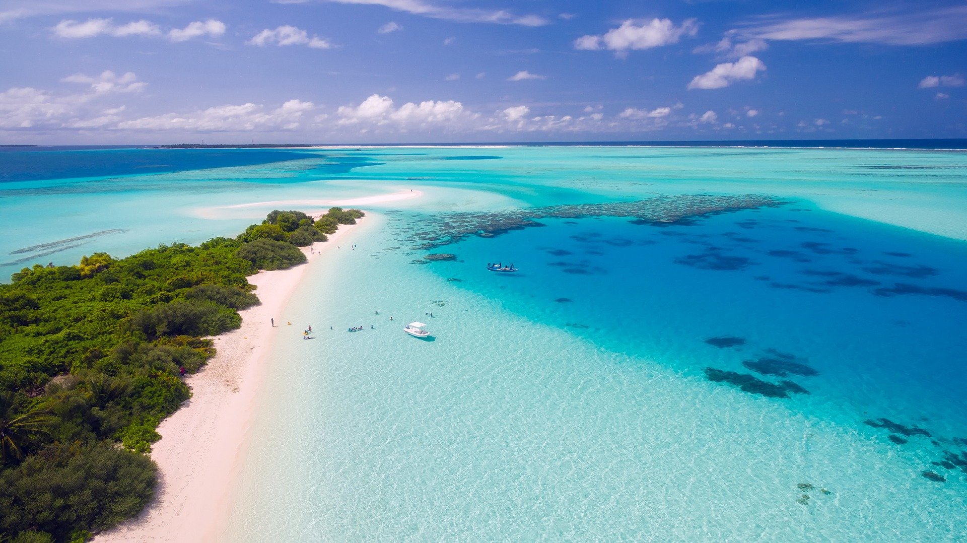 white sand beach and turquoise waters of the Maldives with coral reed and boats visible