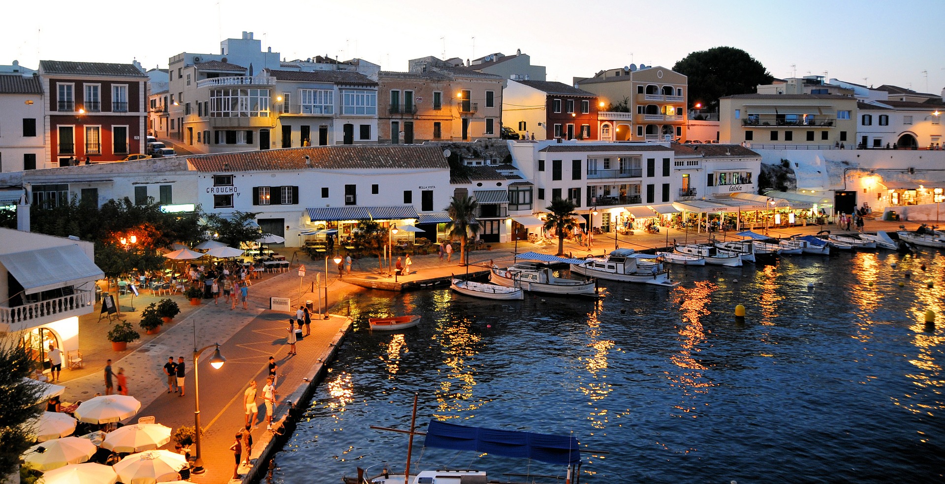 evening shot of harbour in Menorca with lights on the boardwalk and boats at dock