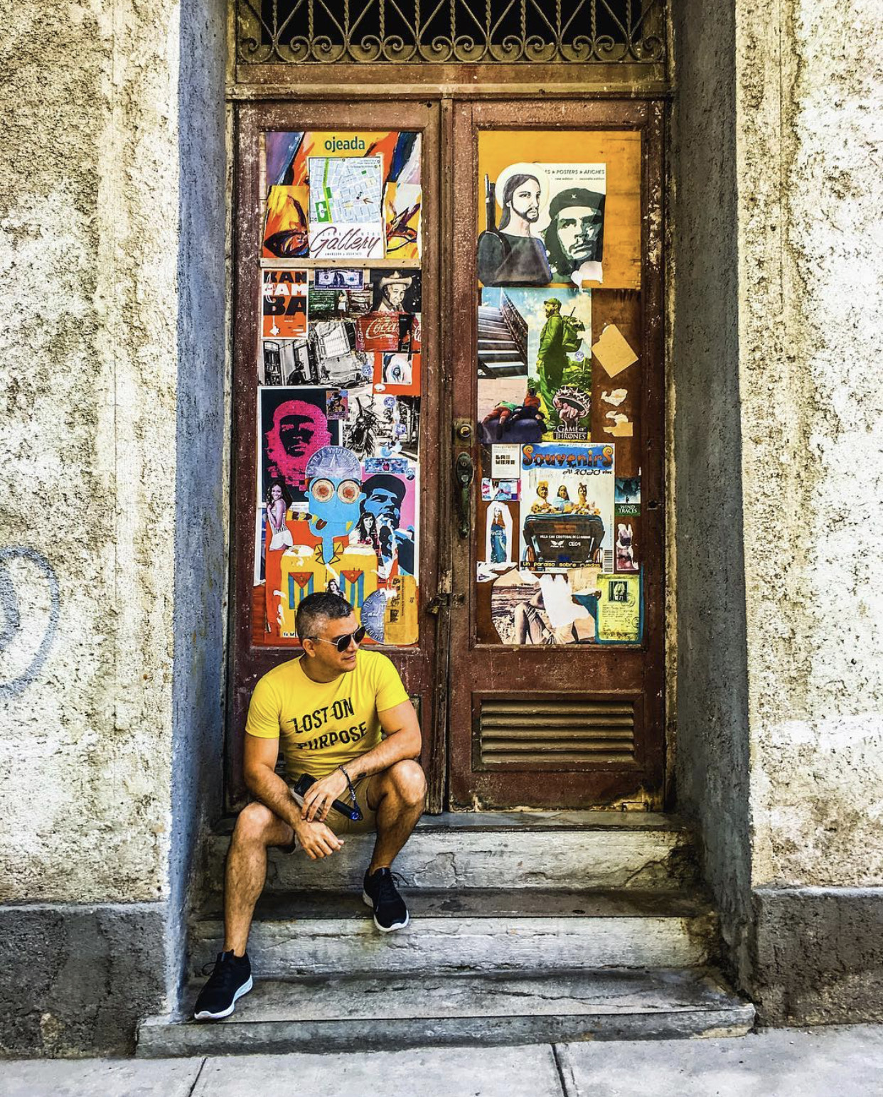 Aruban travel content creator Hyro Oduber sits in front of old doors covered in posters