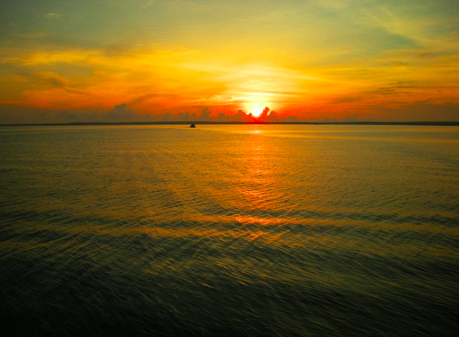 sunset on the Pacific Ocean with tiny boat cruising