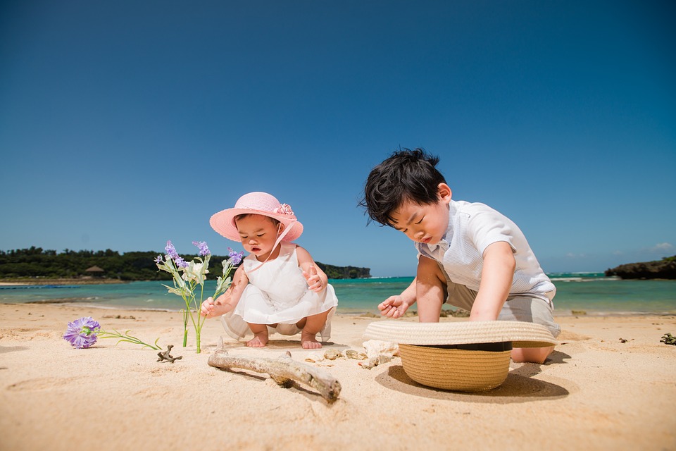 two toddlers play on white sand beach with turquoise waters in the background