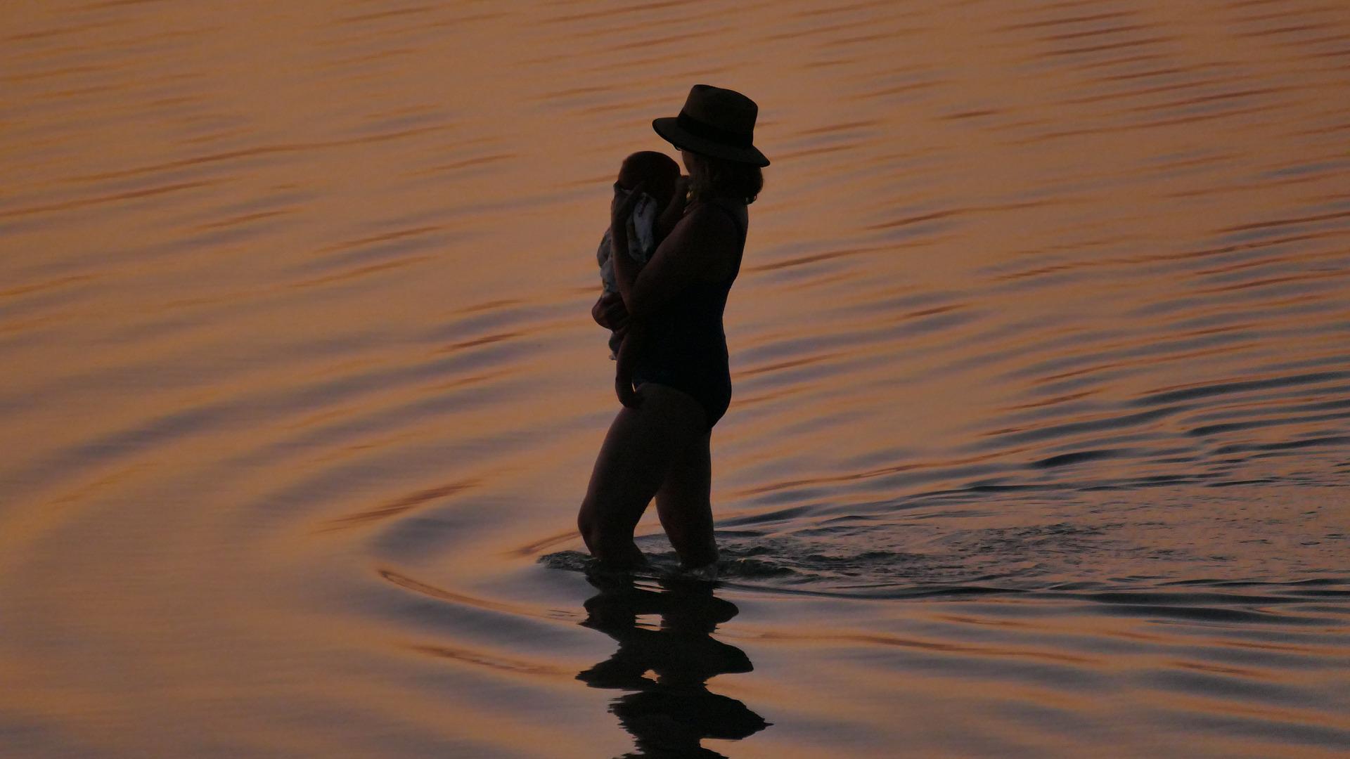 silhouette of mom and baby at sunset in the water